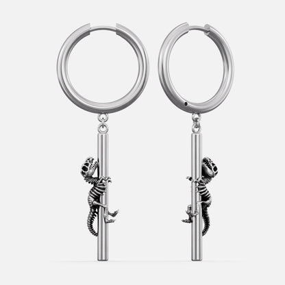Silver-tone hoop earrings with a dangling dinosaur skeleton charm climbing a bar, shown as a pair