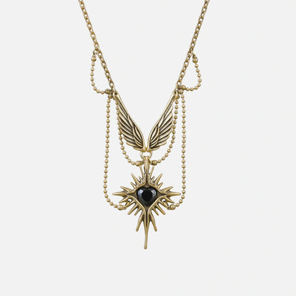 Gold-tone necklace featuring layered chains, wings and a starburst pendant with black stone, laid flat on white background