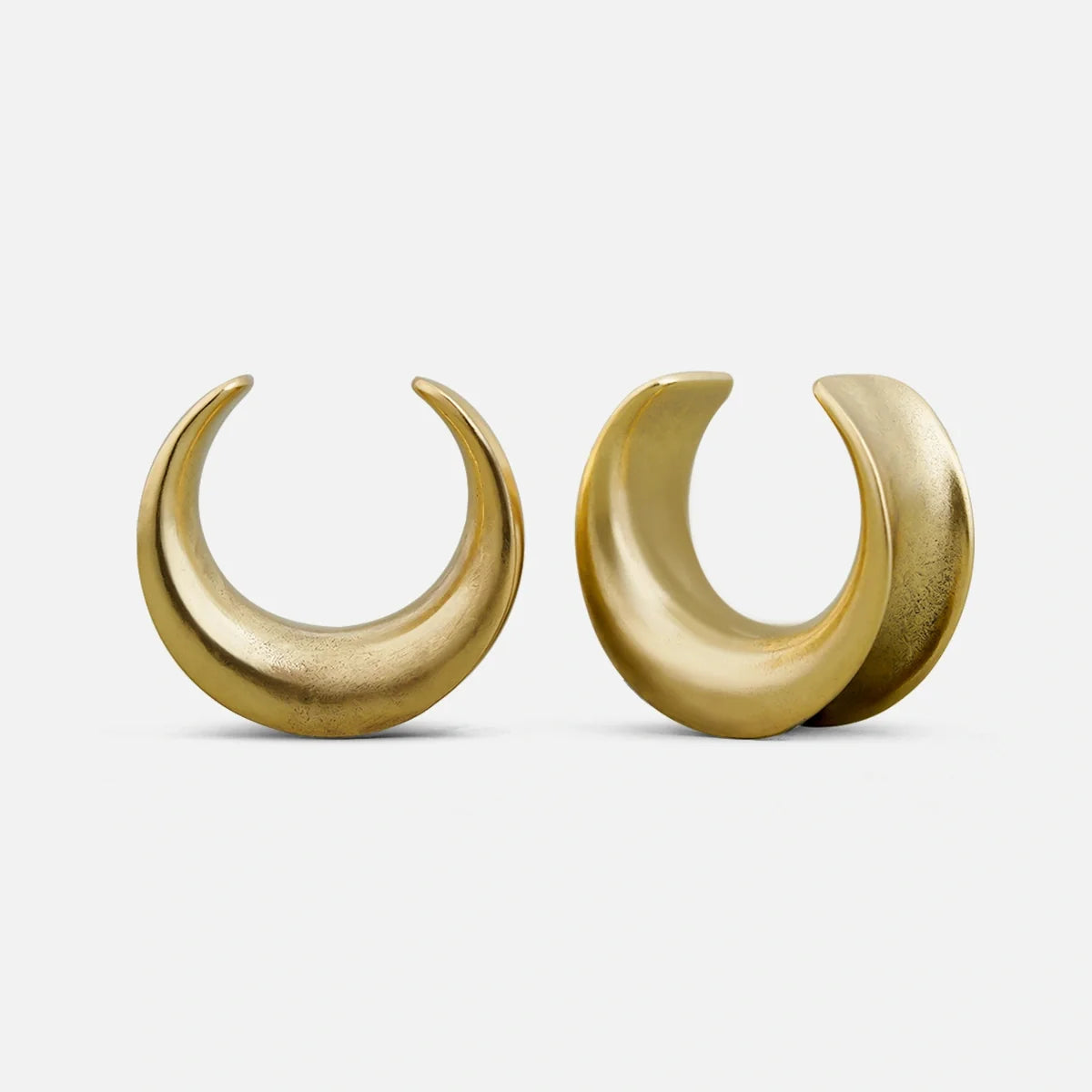 Pair of gold-tone crescent-shaped ear tunnels shown standing side by side against a plain background