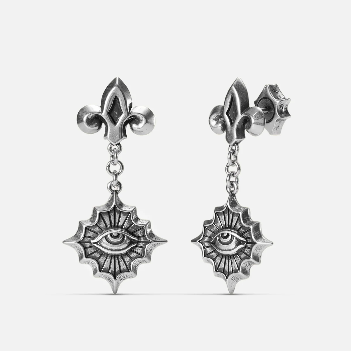 Antiqued silver-tone Radiant Witness Drop Earrings shown from front and side views with sculpted eye motifs, radiating pointed frames, and fleur-de-lis studs.