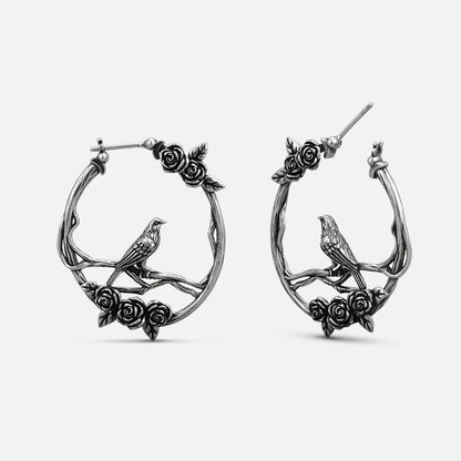 Pair of oxidized silver-tone hoop earrings with rose vine and perched bird design, front view