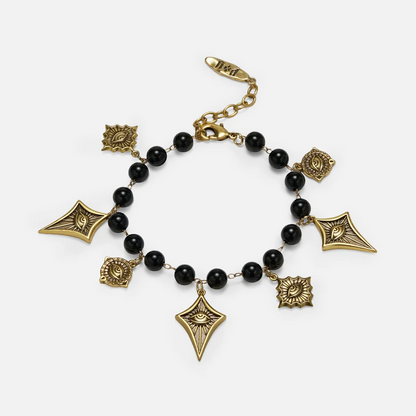 A gold and black beaded charm bracelet featuring geometric and floral charms, displayed on a light gray background.